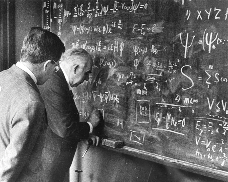 Niels Bohr (right) and son Aage Bohr (left) stand at a blackboard writing equations. Image courtesy of the AIP Emilio Segrè Visual Archives, Margrethe Bohr Collection