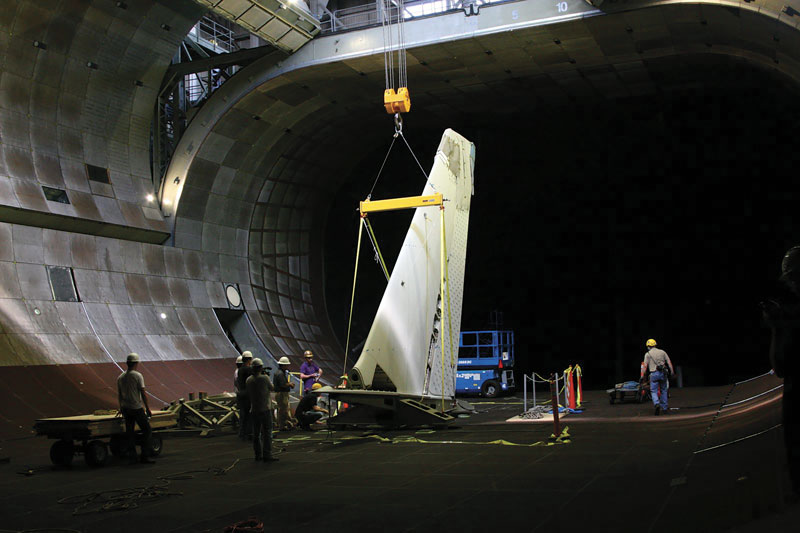 A 40-ton crane carefully lowers AN aircraft tail from the rafters down through the open doors of the tunnel's roof. Photo courtesy of NASA / Eric James.