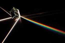White light goes through a prism lying on a black background, refracting into spectral colors. Photo by iStock.com/joephil.